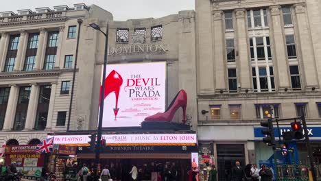 handheld shot of dominion theatre exterior displaying new show: the devil wears prada during a busy day in london.