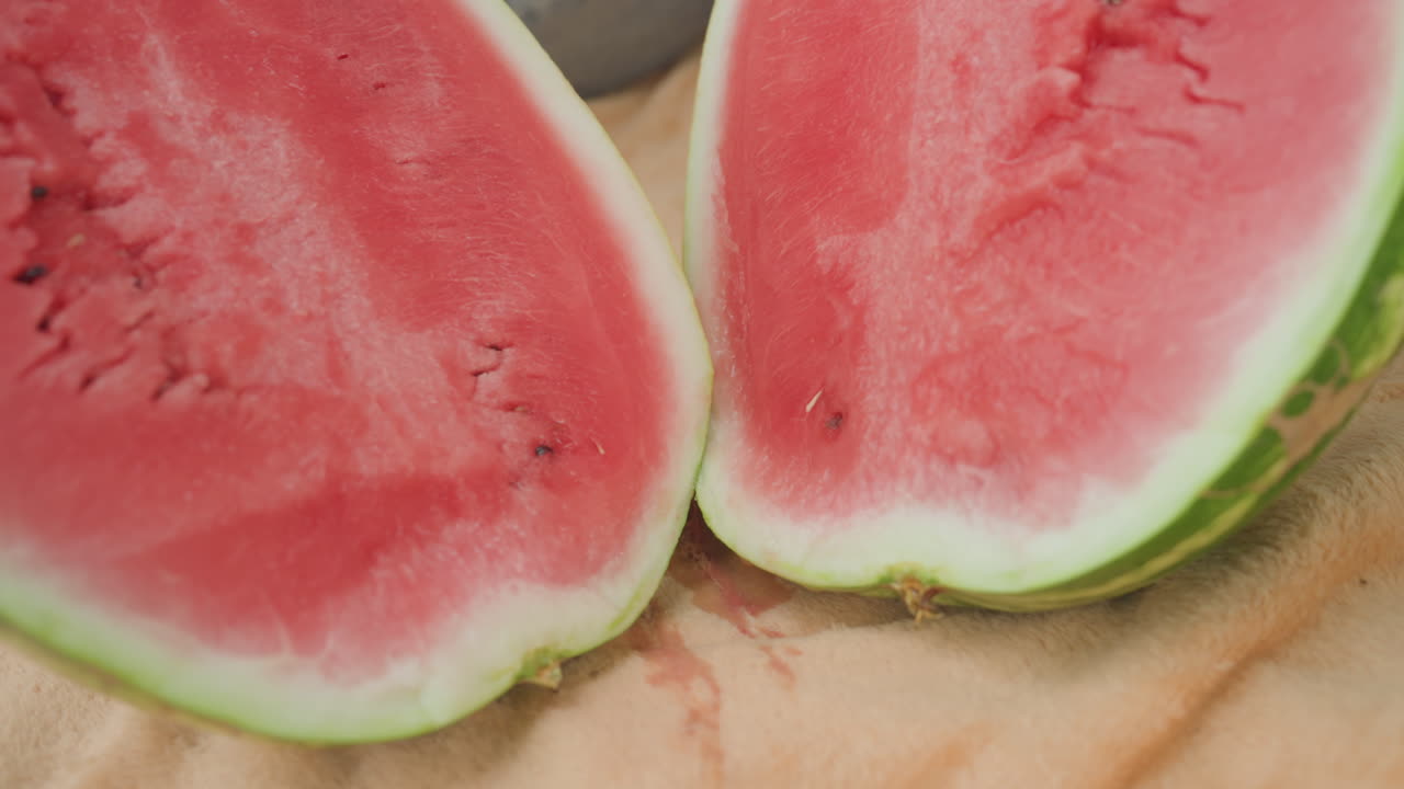 아이들이 수박을 타월 위에서 쪼개고, 손으로 껍질을 눌러 밝은 빨간색 과육과 씨앗을 보이게 하고, 맨발 다리가 근처에 있으며, 칼은 옆에 두고 과즙이 풍부한 과육을 클로즈업하여 보여주는 햇빛 비치는 뒷마당 피크닉 장면