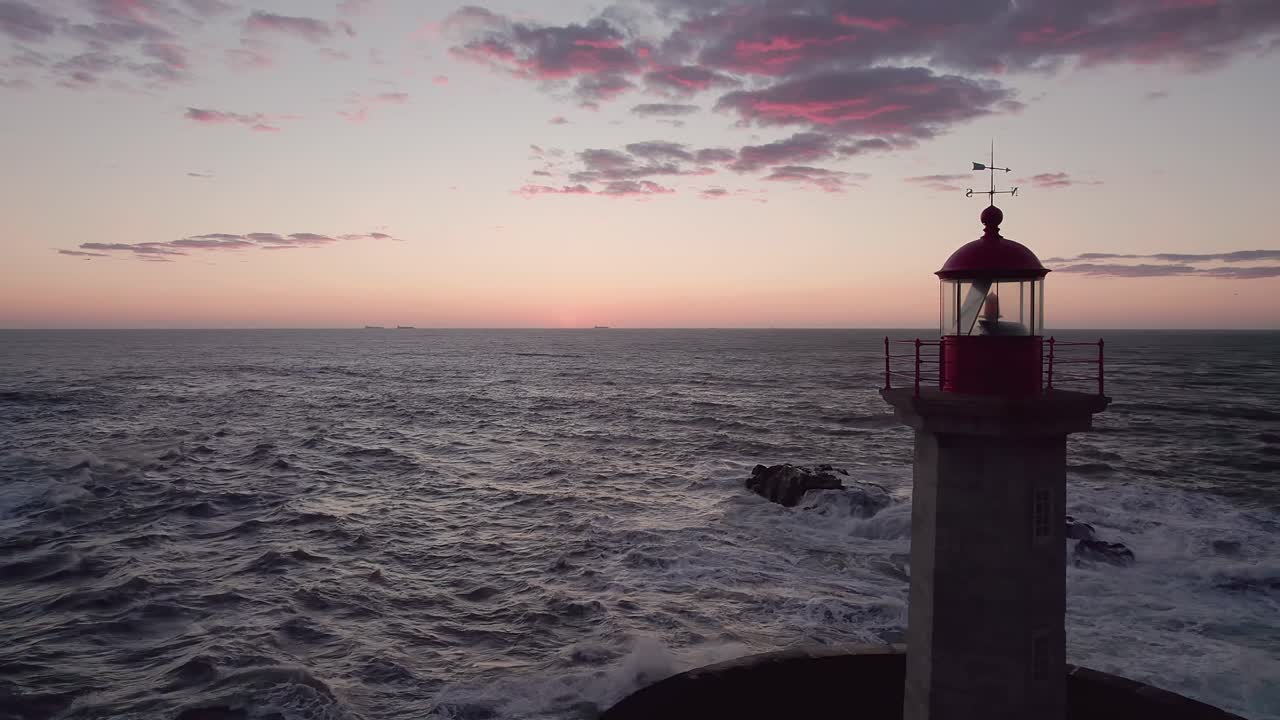Drone performs deliberate slow forward push-in toward Farol da Barra lighthouse on breakwater at Rio Douro mouth, Atlantic waves surrounding structure during golden hour sunset