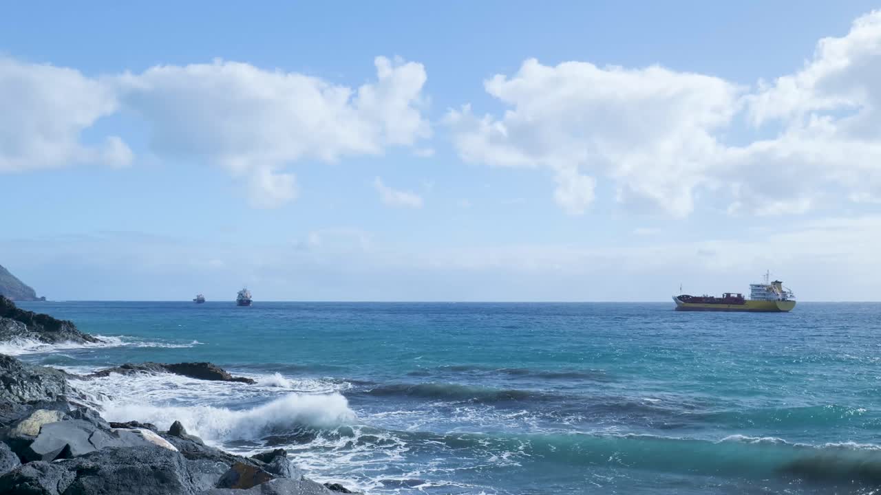 貨物船が浮かぶ岩場の海岸に打ち寄せる波