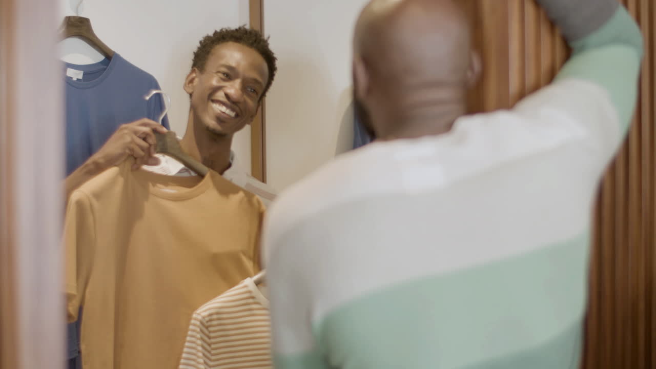 Slender black guy trying on T-shirts in dressing room.