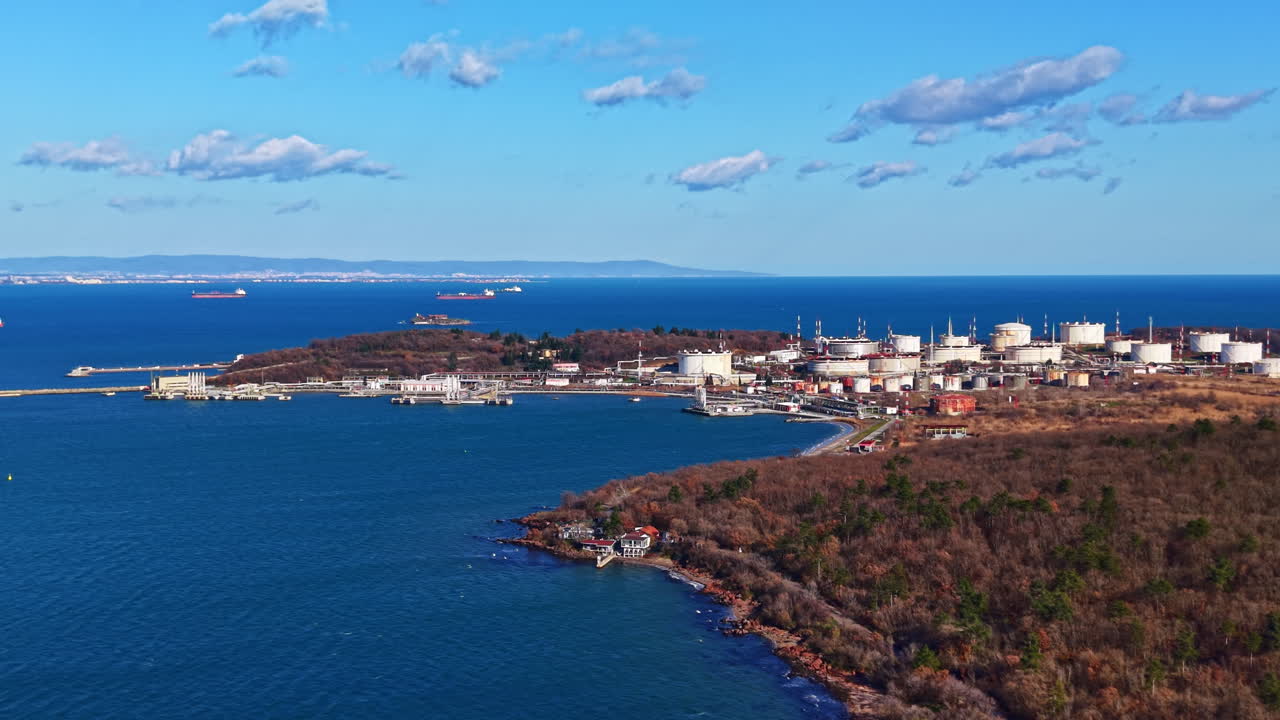 Veduta di un'area industriale marittima con serbatoi di stoccaggio e navi vicino alla costa in una giornata limpida.