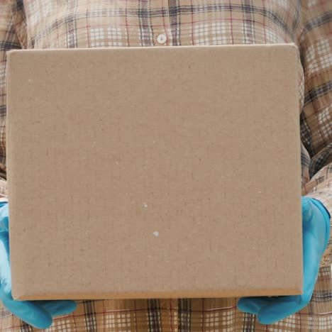 courier with cardboard box in hand stands against the background of the delivery service van