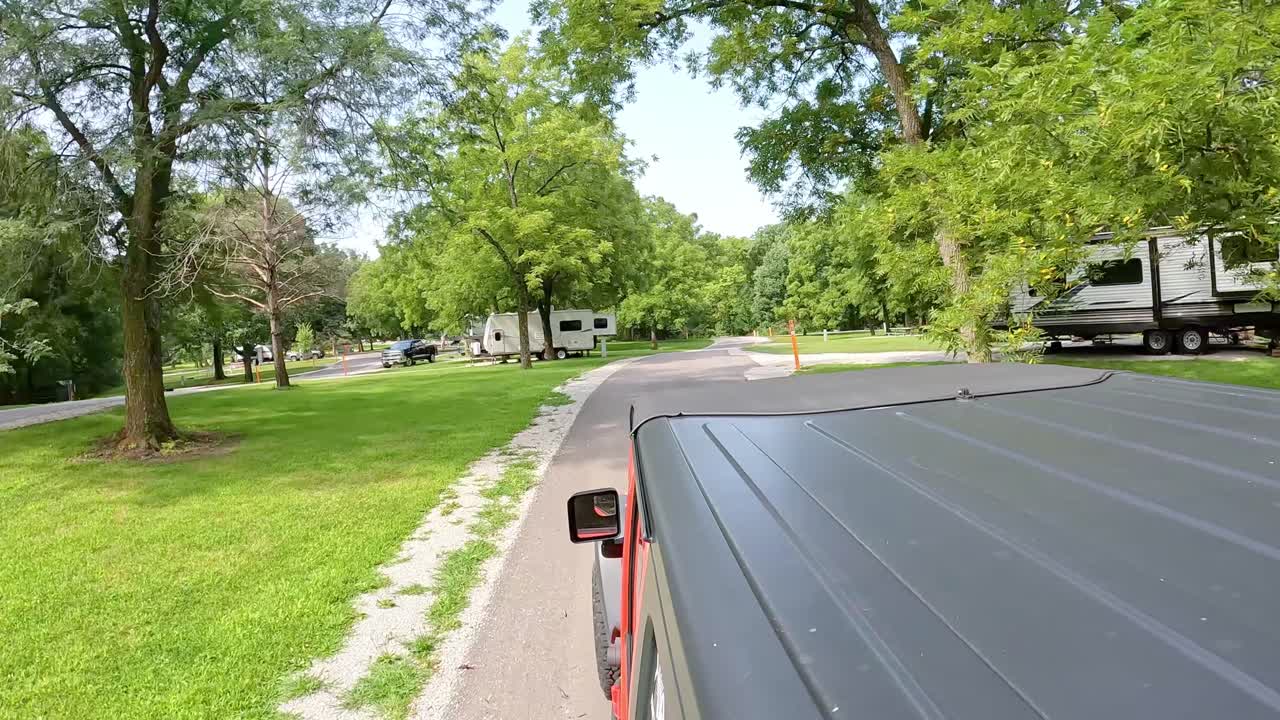 POV from vehicle roof - driving on road thru park with campground in Central Iowa; driving past recreational vehicles and trailers in late summer in the Des Moines River valley; vacation, holiday