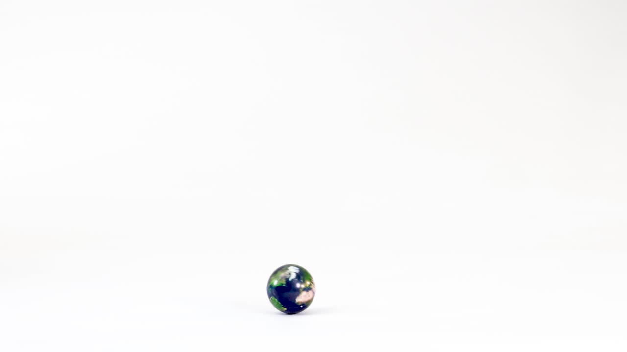 A small rubber ball with a world map pattern rolls across a white studio floor