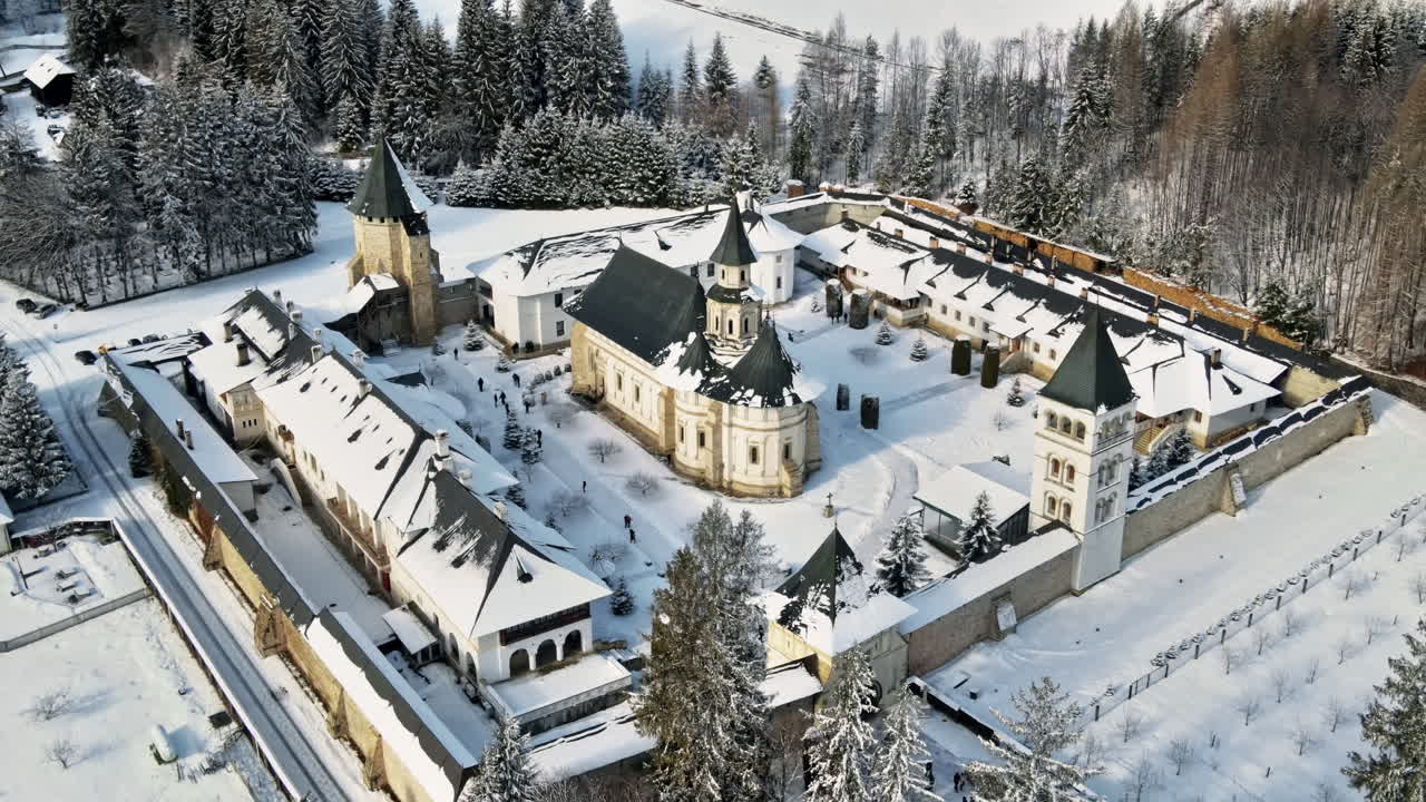 Letecký pohled dronem na klášter Putna v zimě, Rumunsko. Vnitřní nádvoří s procházejícími se turisty, holé stromy, sníh, kopce v okolí