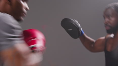 real time studio shot of male boxer sparring working out with trainer wearing punch mitts or gloves practising for fight