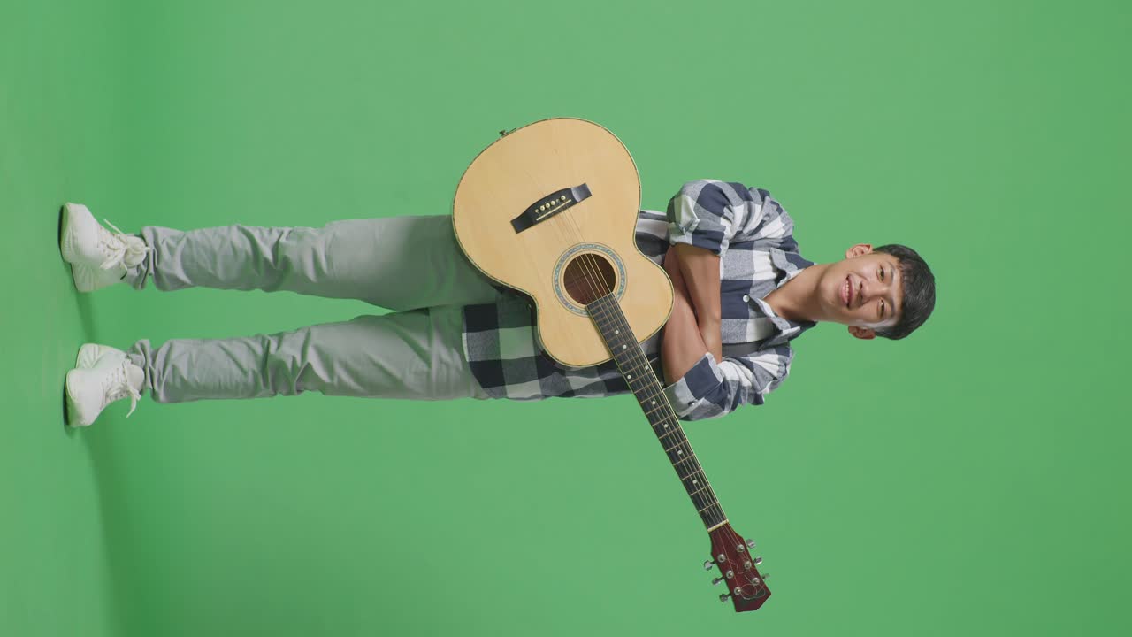 Full Body Of Asian Teenager With Guitar Crossing His Arms And Smiling On Green Screen Background