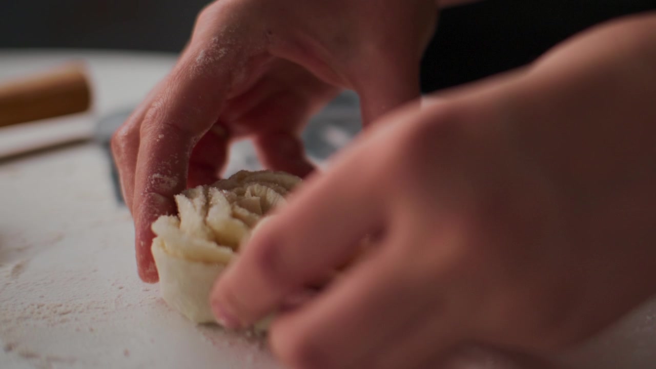 Primo piano di mani che modellano l'impasto su una superficie infarinata. Le dita premono e modellano l'impasto con cura e concentrazione. L'illuminazione soffusa evidenzia la consistenza e il movimento. Ideale per cucinare, cuocere al forno.