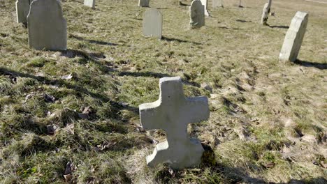 cemetery with many headstones scattered throughout a grassy field, with a cloudy sky in the background, long shadows, pans up