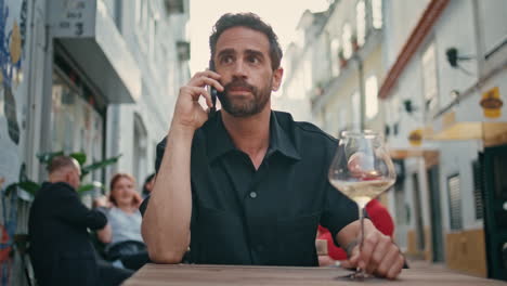 hombre nervioso hablando con su teléfono inteligente en un bar urbano de cerca. hombre de negocios con vino en la mano