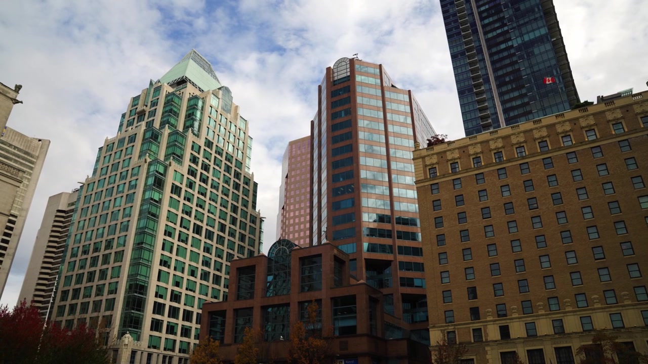 Foto de paisagem em grande angular de uma variedade de edifícios e arranha-céus no centro de Vancouver, na Georgia Square. Algumas construções com design moderno e novo, bem como edifícios históricos de tijolos icônicos.