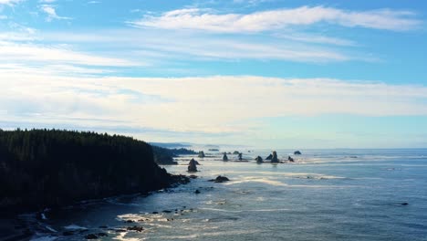 Stunning-descending-aerial-drone-shot-of-the-gorgeous-Third-Beach-in-Forks,-Washington-with-large-rock-formations,-cliffs,-small-waves-and-sea-foam-on-a-warm-sunny-summer-morning