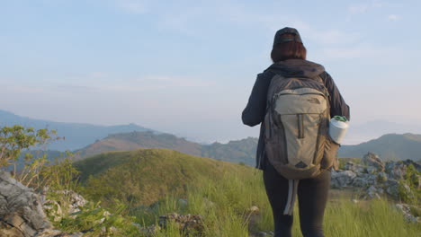 toma trasera de una joven mochilera acercándose a la cumbre de la montaña