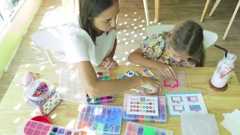 mother and daughter doing a beading craft in a cafe