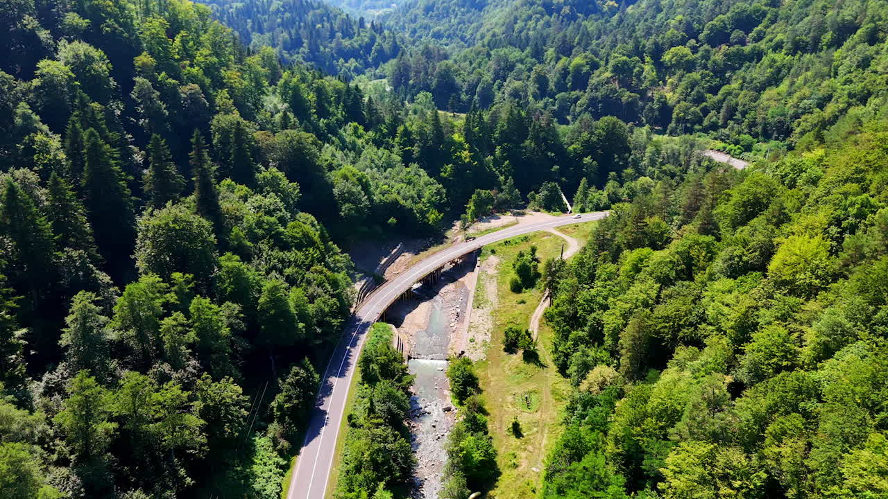 Curving road above forested valley. A winding road arcs over a lush green valley with a river flowing below