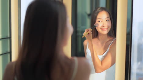 beautiful asian woman in mirror putting on make up with soft brush