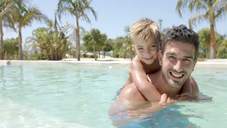 Portrait-of-happy-caucasian-father-carrying-his-son-in-swimming-pool