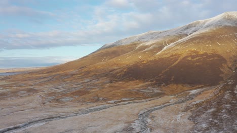 Iceland-scenic-aerial-view-of-snowy-mountain-panning-towards-frozen-delta-river,-sunset