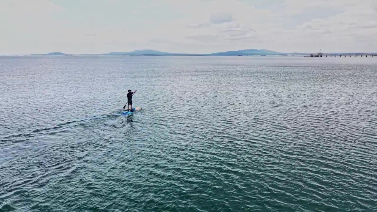 Un paddleboarder glisse sur une eau calme près du rivage par temps couvert.