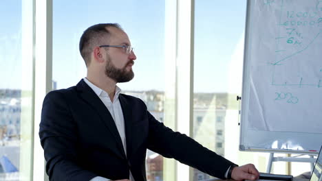 bearded business worker in glasses in office center. successful office worker in elegant costume sitting at his workplace near the window and speaking.