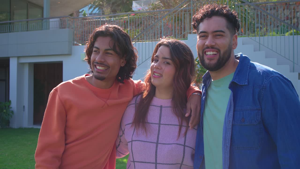 Amigos hispânicos vendo a câmera virar e olhando para a lente, rindo no quintal de uma casa moderna