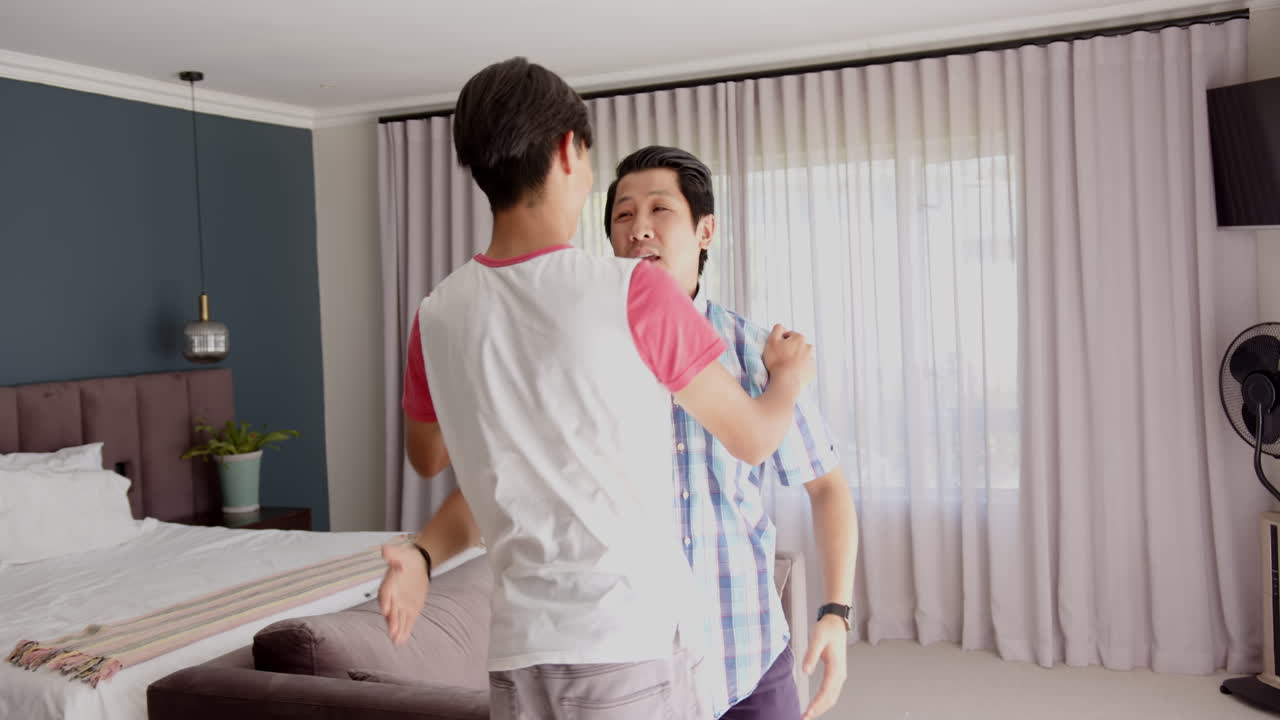 Asian father and teenage son standing together in modern living room