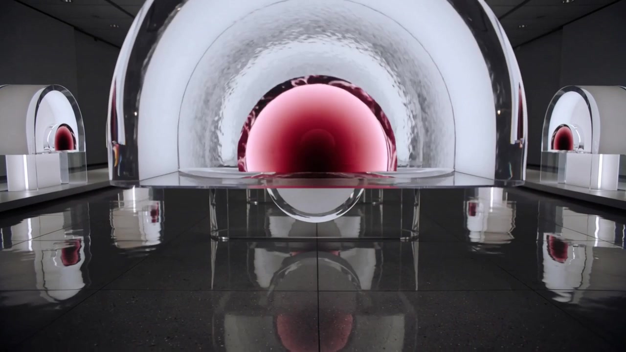 La telecamera si allontana, rivelando una cupola trasparente con un nucleo rosso su una base di vetro, che mostra archi illuminati e simmetria.
