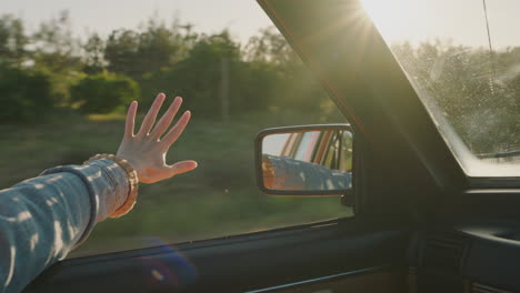 woman holding hand out car window feeling wind blowing through fingers driving in countryside travelling on summer vacation road trip enjoying freedom on the road