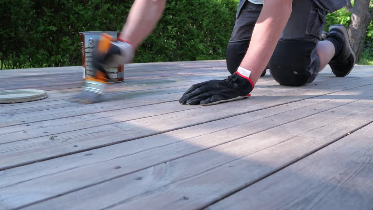 il proprietario di casa tratta la pavimentazione in legno con olio di pavimentazione usando un pennello