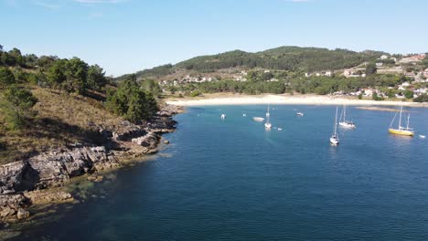 aerial view of liméns beach, overlooking the calm blue waters of the ría de vigo. secluded sandy beach, surrounded by dense green forests and coastal sailor villages nestled in the hills.
