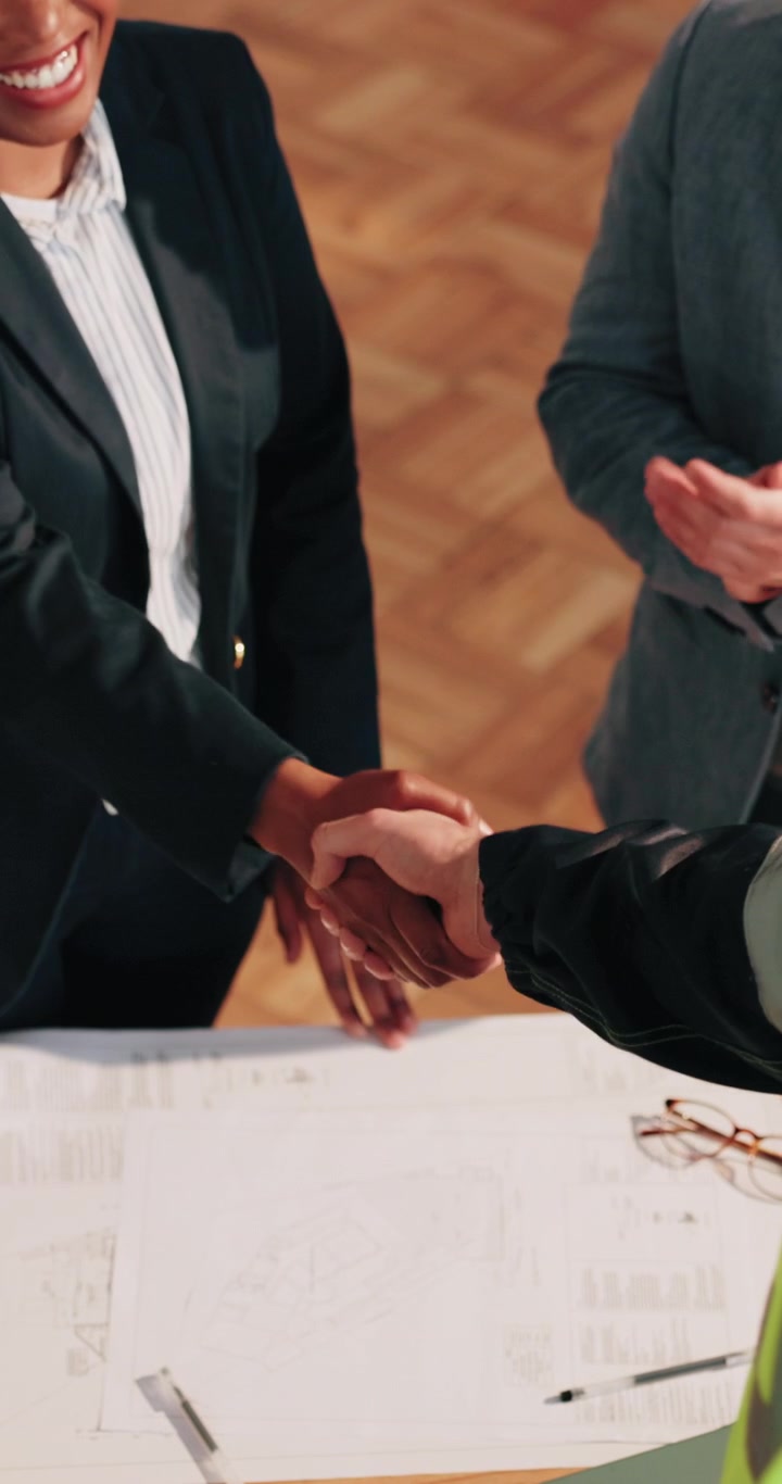 Profesionales de negocios dándose la mano sobre planos arquitectónicos