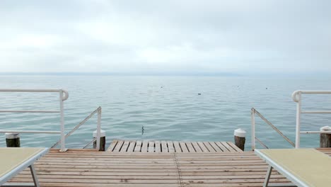 el tiro de empujón desde la cubierta de sol retro del muelle de madera revela el azul y tranquilo ambiente del lago garda.
