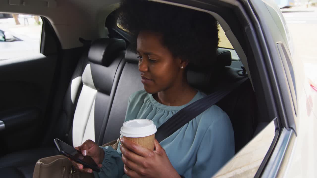African american businesswoman using smartphone and holding takeaway coffee in car