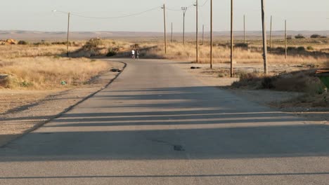 Static-footage-of-a-single-road-with-old-power-poles-in-the-middle-of-the-desert-near-a-military-base-as-two-soldiers-run-in-the-background