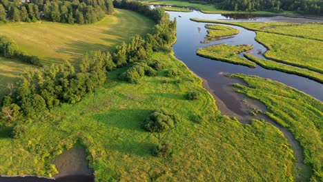 cinematic-view-from-a-drone,-while-rotating-over-a-wide-river-that-flows-through-the-green-nature-below-the-mountains