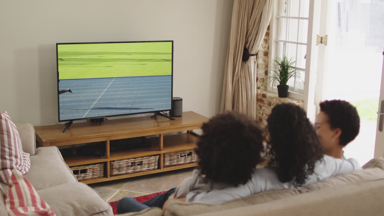 compuesto de una familia feliz sentada en casa juntos viendo un evento de atletismo en la televisión