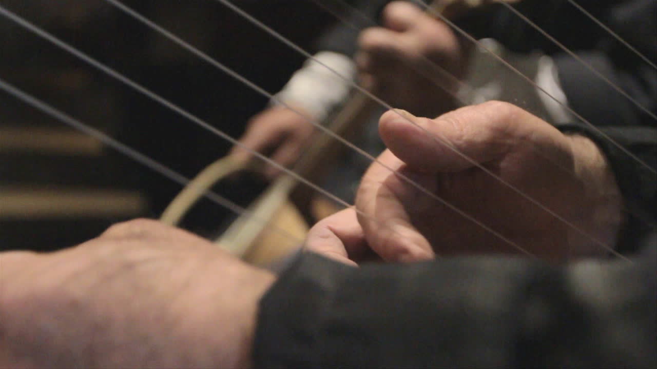 Close up of hands playing a traditional Georgian harp and the chuniri string instrument, with wrack focus on both instruments