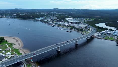 drone aerial shot over batemans bay bridge cars highway with rural town shops commercial infrastructure clyde river south coast australia