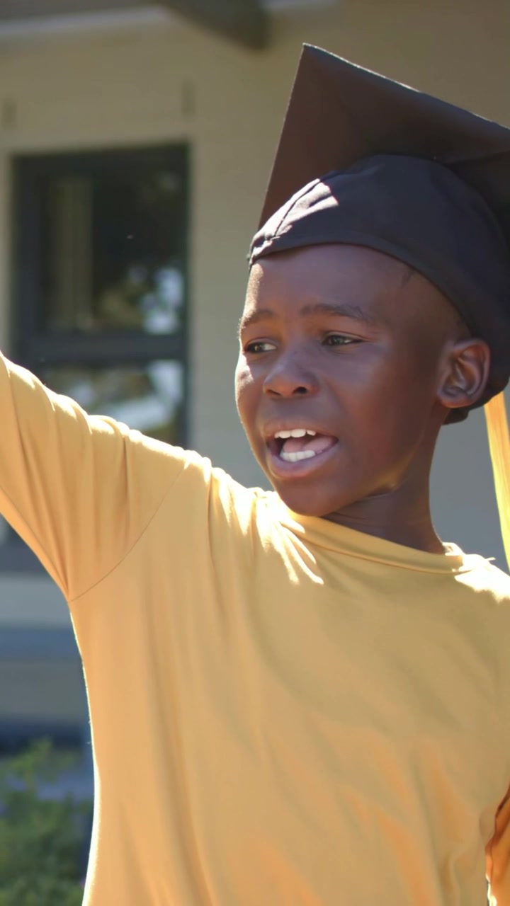 Vertical video: Focusing raised arm, boy waving diploma, calling at school in cap, copy space