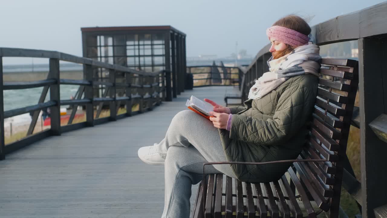Kvinde læser en bog på en træbænk ved stranden