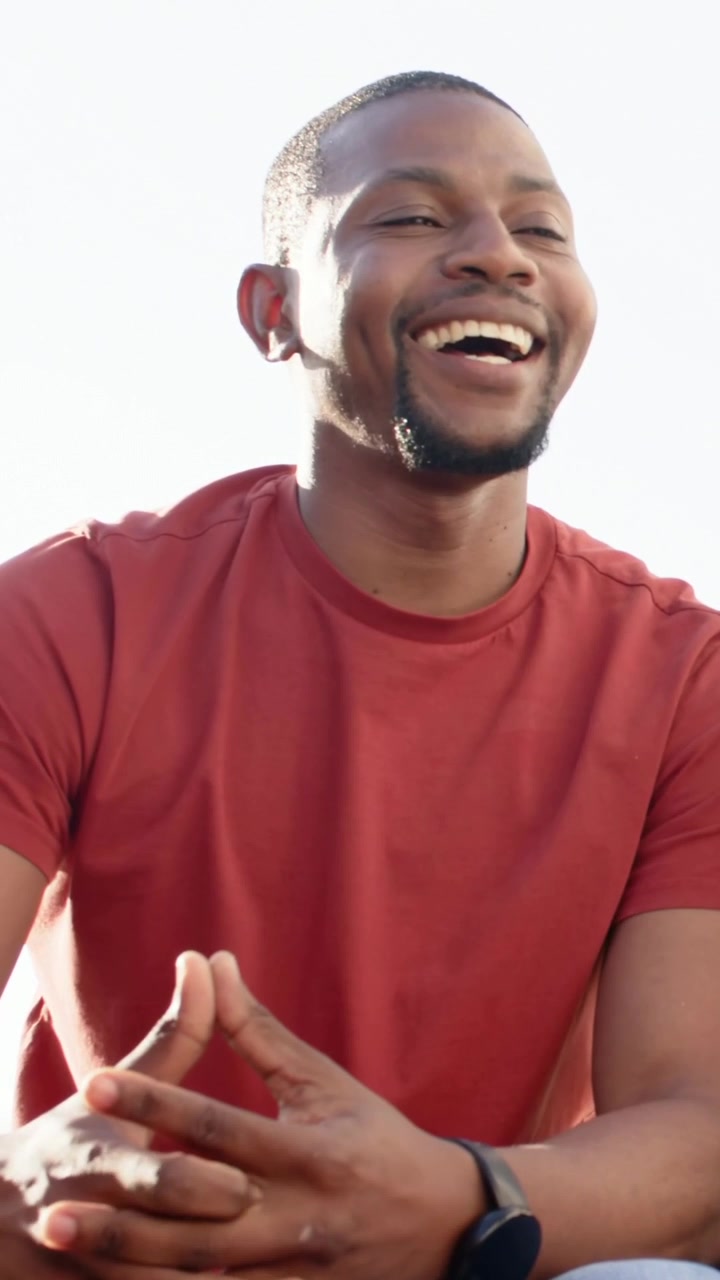 Vertical video: Gaze shifting right, man in red tee laughing, settling outside, dark smartwatch