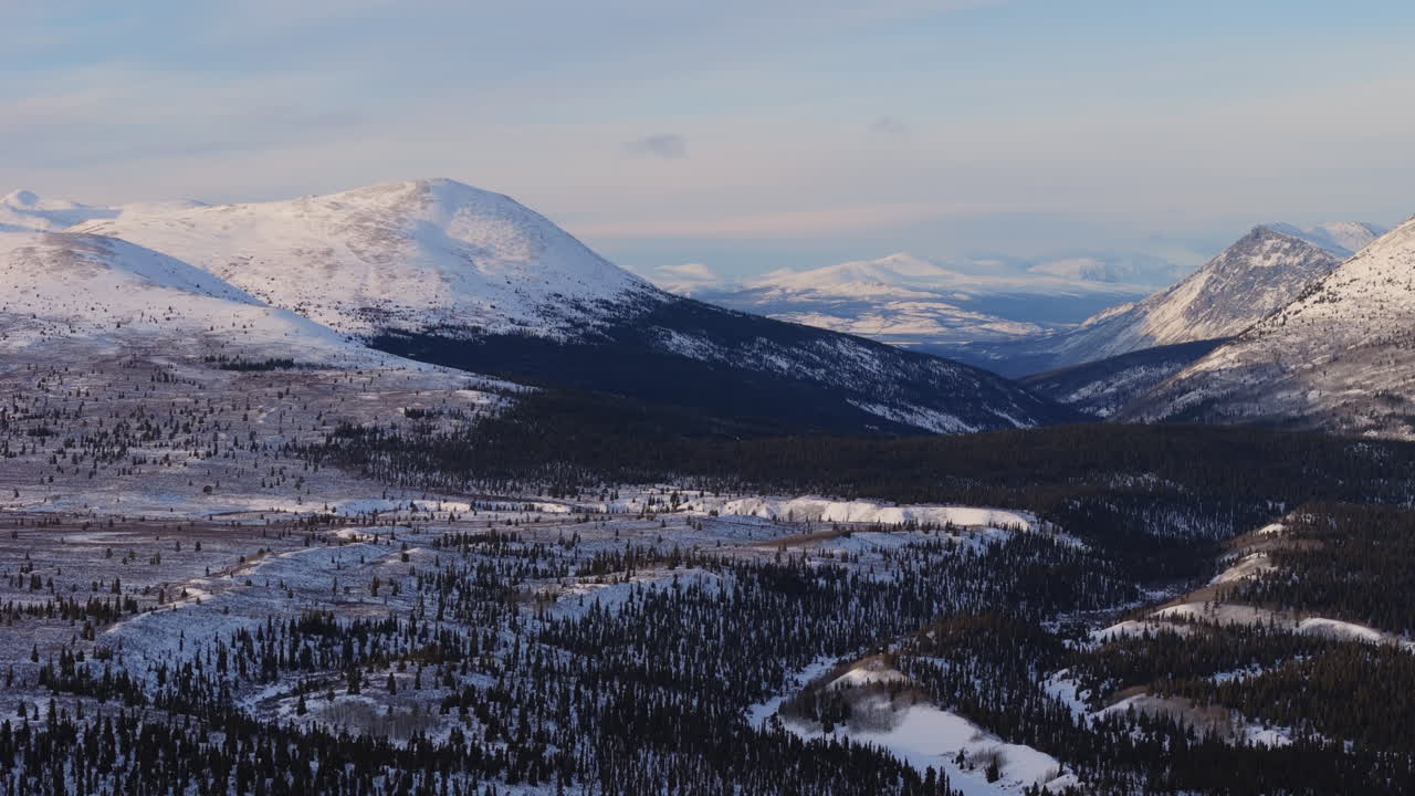A cinematic aerial view of Mountain Landscape near Fish Lake at sunset. Golden hour light enhances the frosty Yukon wilderness, showcasing a pristine snow-covered winter scene.