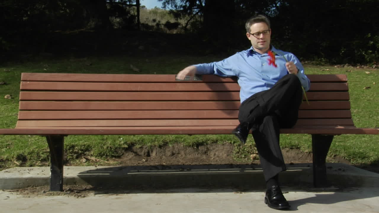 un hombre se sienta solo en un banco del parque con dos flores