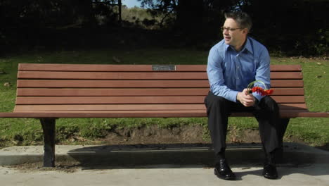 A-man-sits-alone-on-a-park-bench-with-two-flowers