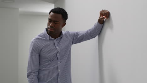 young man with mental health issues standing leaning against wall in office looking depressed and unhappy 1