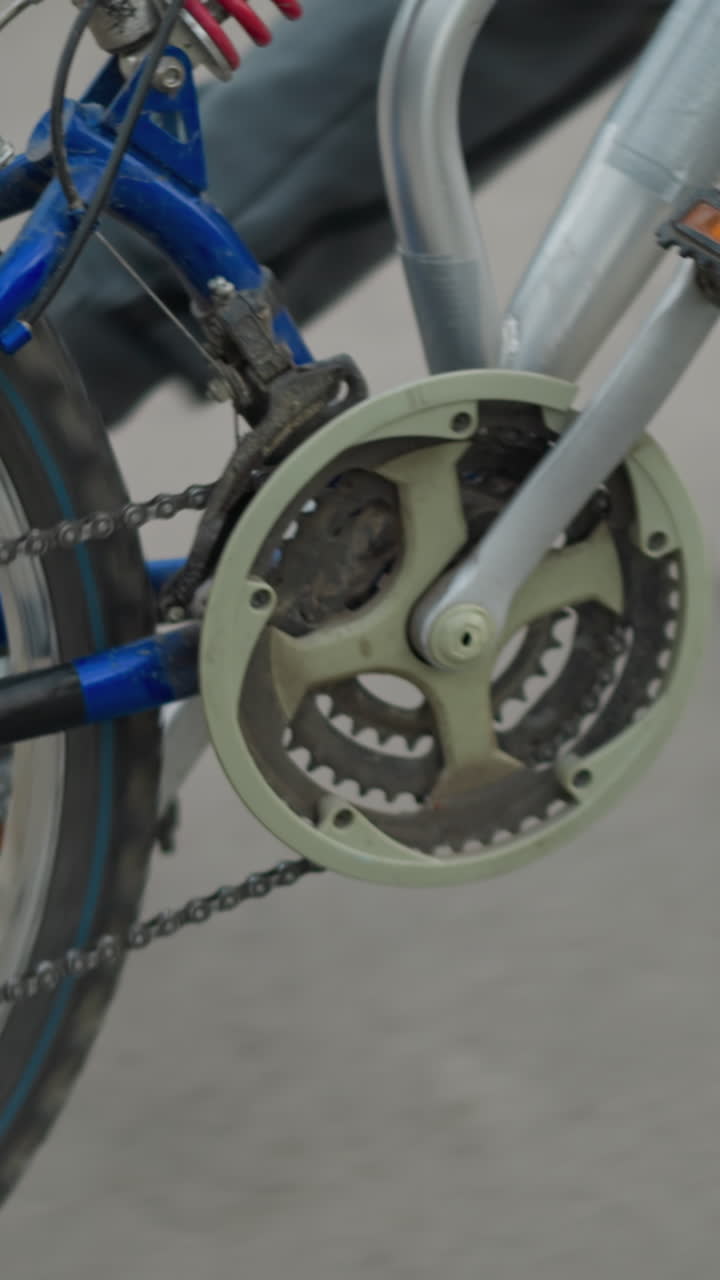 회색 바지를 입은 사람, 검은 스니커를 입은 사람이 색으로 칠한 보행자 교차로를 가로질러 그와 함께 는 자전거 체인과 페달의 클로즈업