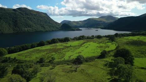 Flying-over-wooded-fields-towards-dark-lake-surrounded-by-wooded-mountains-on-bright-summer-day