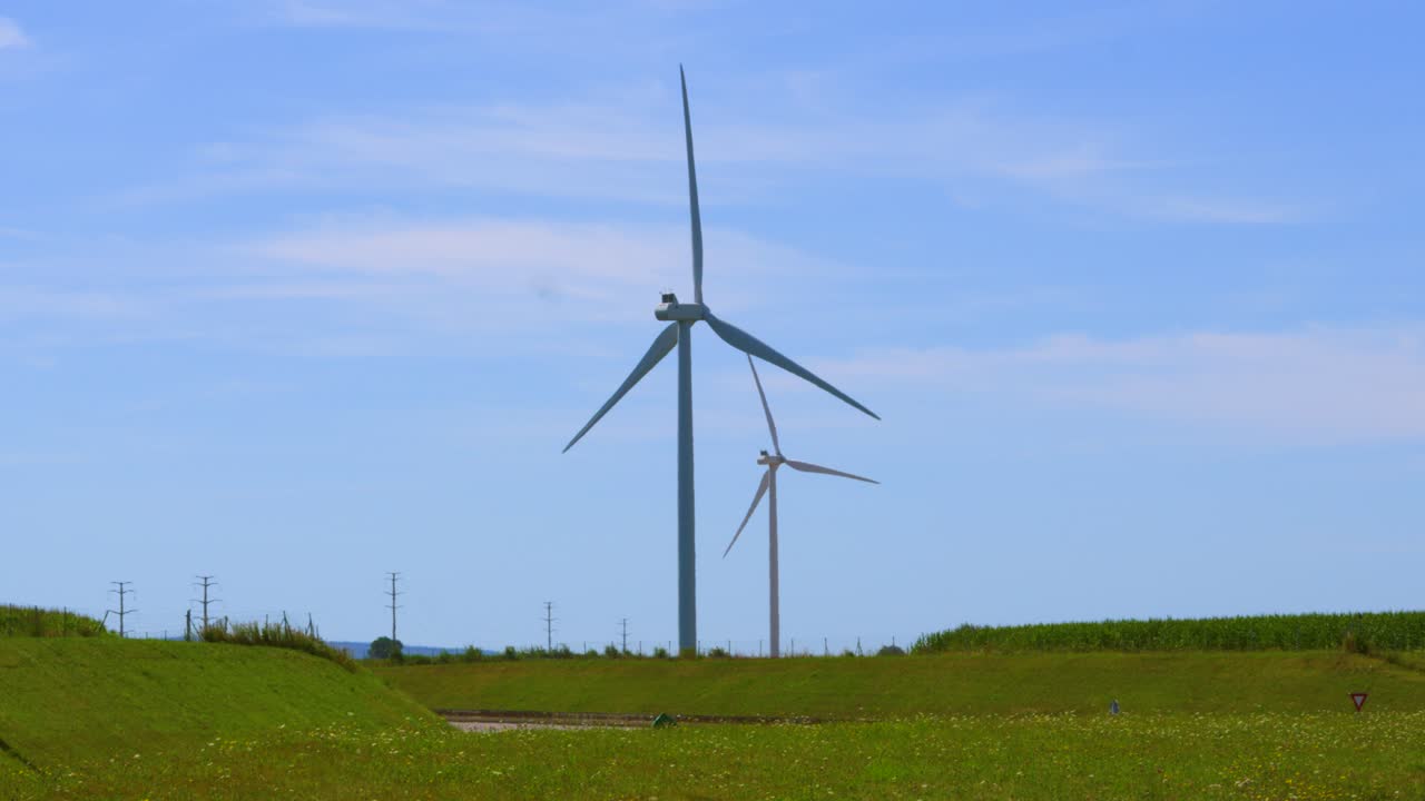 turbinas eólicas de energía limpia renovable girando en cámara lenta junto a la carretera con automóviles y pilares eléctricos en el fondo con cielo azul en verano 4k