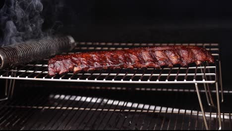 a low angle pan of smoking pork baby back ribs run and sauce